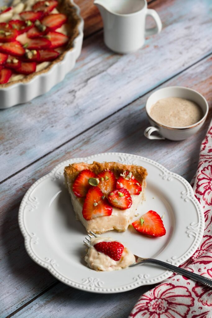 Ein Stück Erdbeer-Tarte am Teller mit Kaffee serviert.